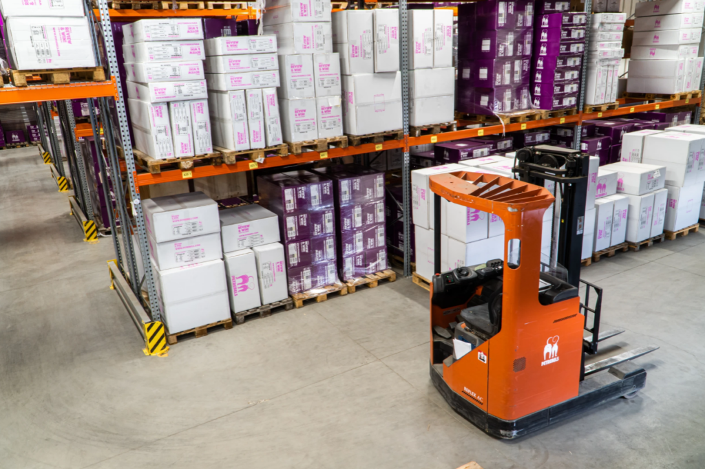 An Orange Forklift in the Warehouse With Packages on Shelves